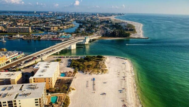 Vista aérea de una zona costera con playa, un puente y un puerto deportivo.