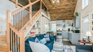 A spacious living area with a blue sofa, a wooden staircase, and a kitchen in the background.