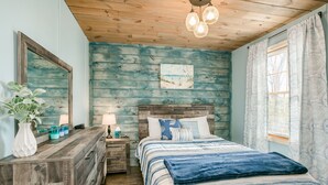 A bedroom with a wooden ceiling, a bed with blue bedding, a nightstand with a lamp, and a large mirror.