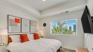 Une chambre avec un grand lit, une fenêtre avec des stores, un téléviseur à écran plat et des œuvres d’art accrochées au mur.