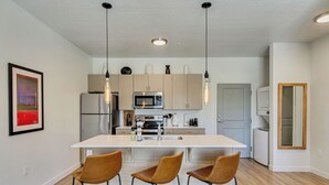 Une cuisine moderne dotée d’un îlot central, de tabourets de bar, d’appareils électroménagers en acier inoxydable et de luminaires suspendus.