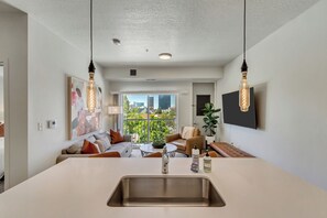 Ein modernes Wohnzimmer mit einer zentralen Insellösung, einem Sofa, einem Couchtisch und Blick auf die Stadt.