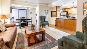 A living room with a sofa, armchair, and coffee table, a dining area with a table and chairs, and a kitchen with wooden cabinets and appliances. - Shadow Ridge 204 | Walk to Lifts | Kitchen | Fireplace | Pool & Hot Tub | Sauna | Fitness Room (Park City)