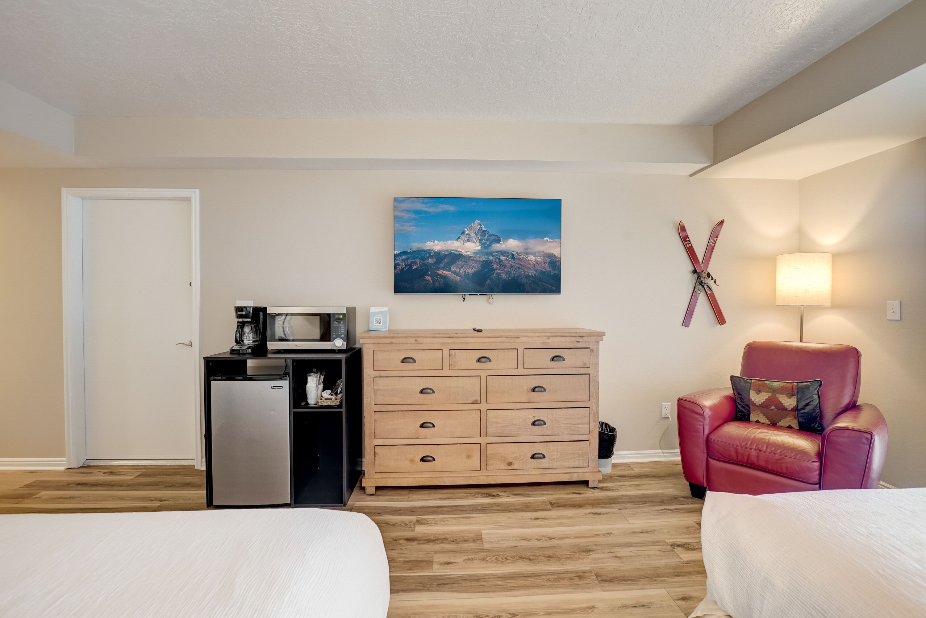 Habitación de hotel con dos camas, un aparador de madera, microondas, refrigerador, televisor montado en la pared y una decoración con temática de esquí.