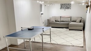 A room with a ping pong table, a grey sofa, and a patterned rug.