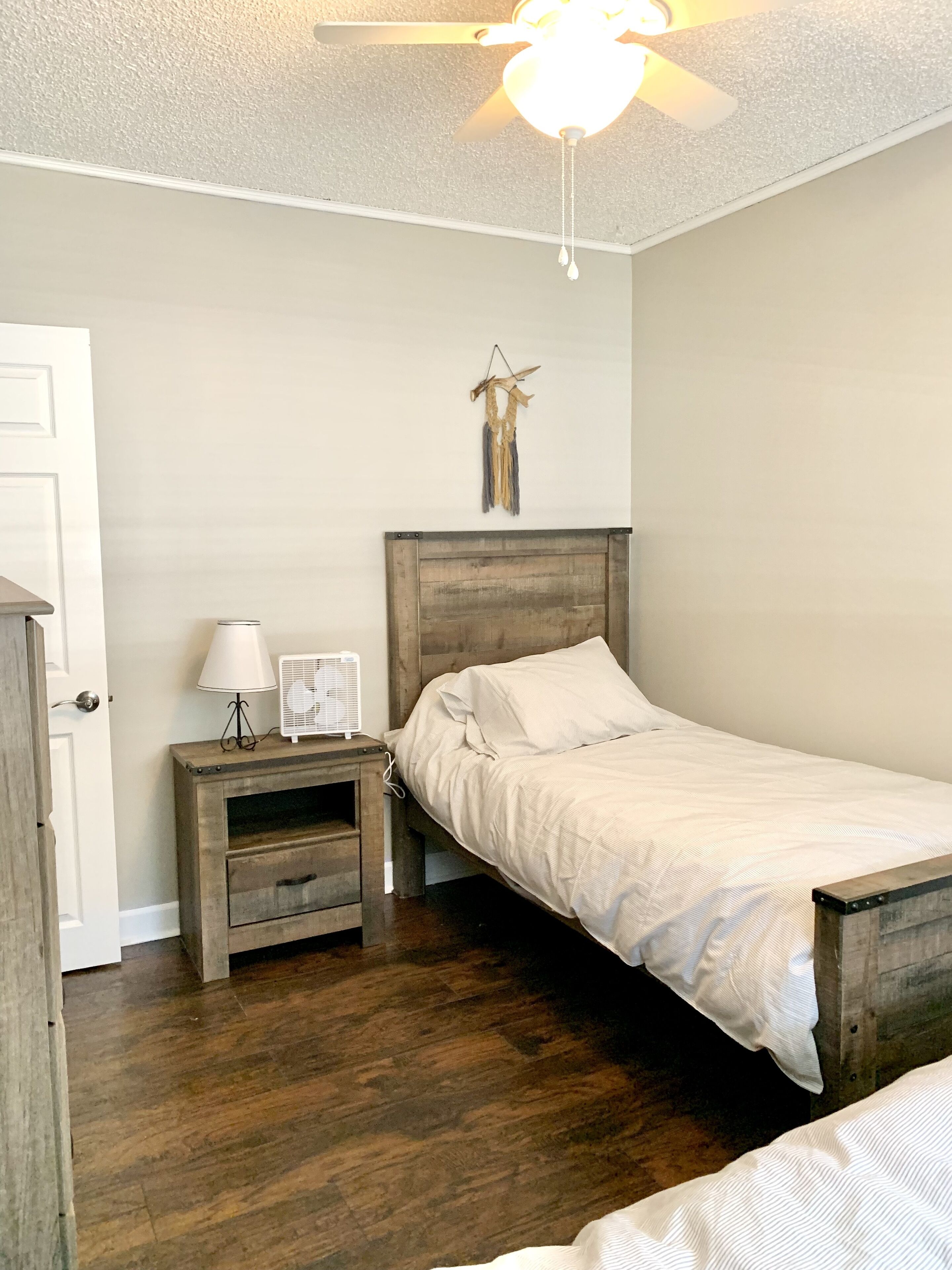 Une chambre à coucher avec un lit en bois, une table de chevet avec une lampe, un ventilateur fixé au mur et un ventilateur de plafond.