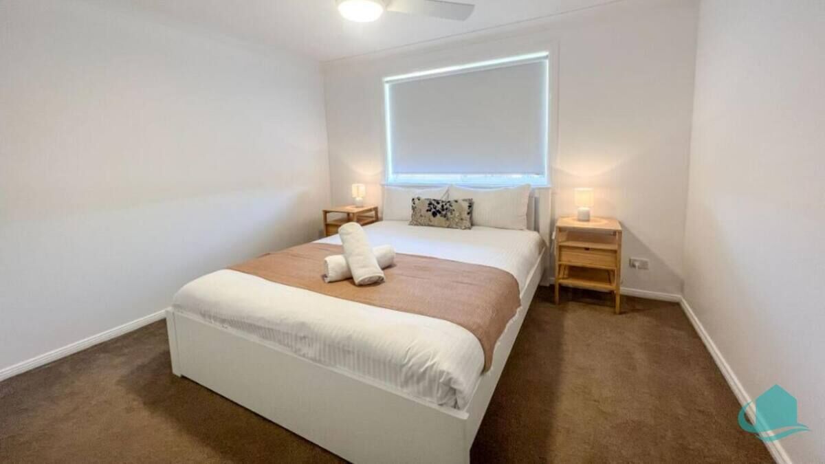 Ein Schlafzimmer mit einem Bett, Nachttischen, einem Deckenventilator und einem Fenster mit Jalousien.