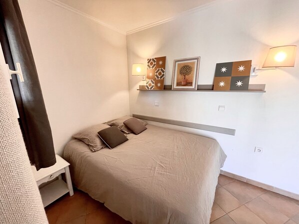 Ein Schlafzimmer mit einem Bett, einem Nachttisch, einer Wandablage mit Dekoration und einer Lampe.