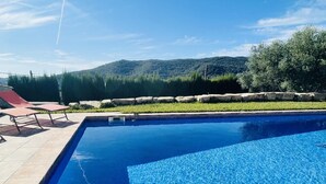 A swimming pool with clear blue water, surrounded by a stone wall and a grassy area. - Villa Loralil by Costabravaway (calonge)