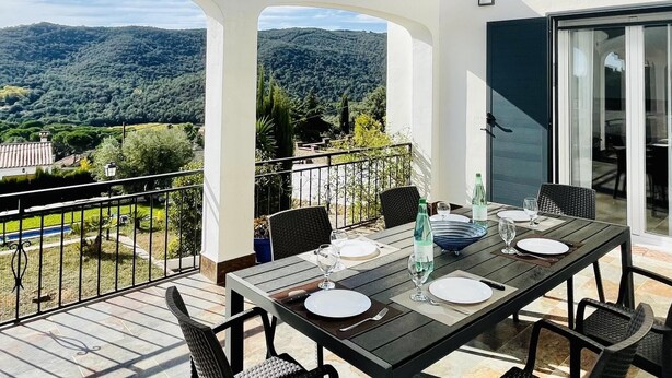 A balcony with a table set for dining, overlooking a mountainous landscape. - Villa Loralil by Costabravaway (calonge)