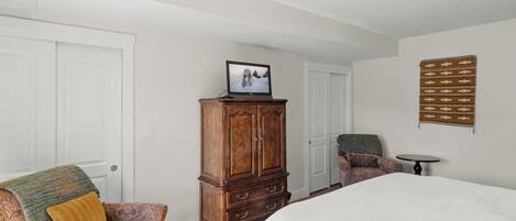 Une chambre à coucher avec un grand lit, une armoire en bois, un fauteuil à motifs, une petite table et une tapisserie murale.