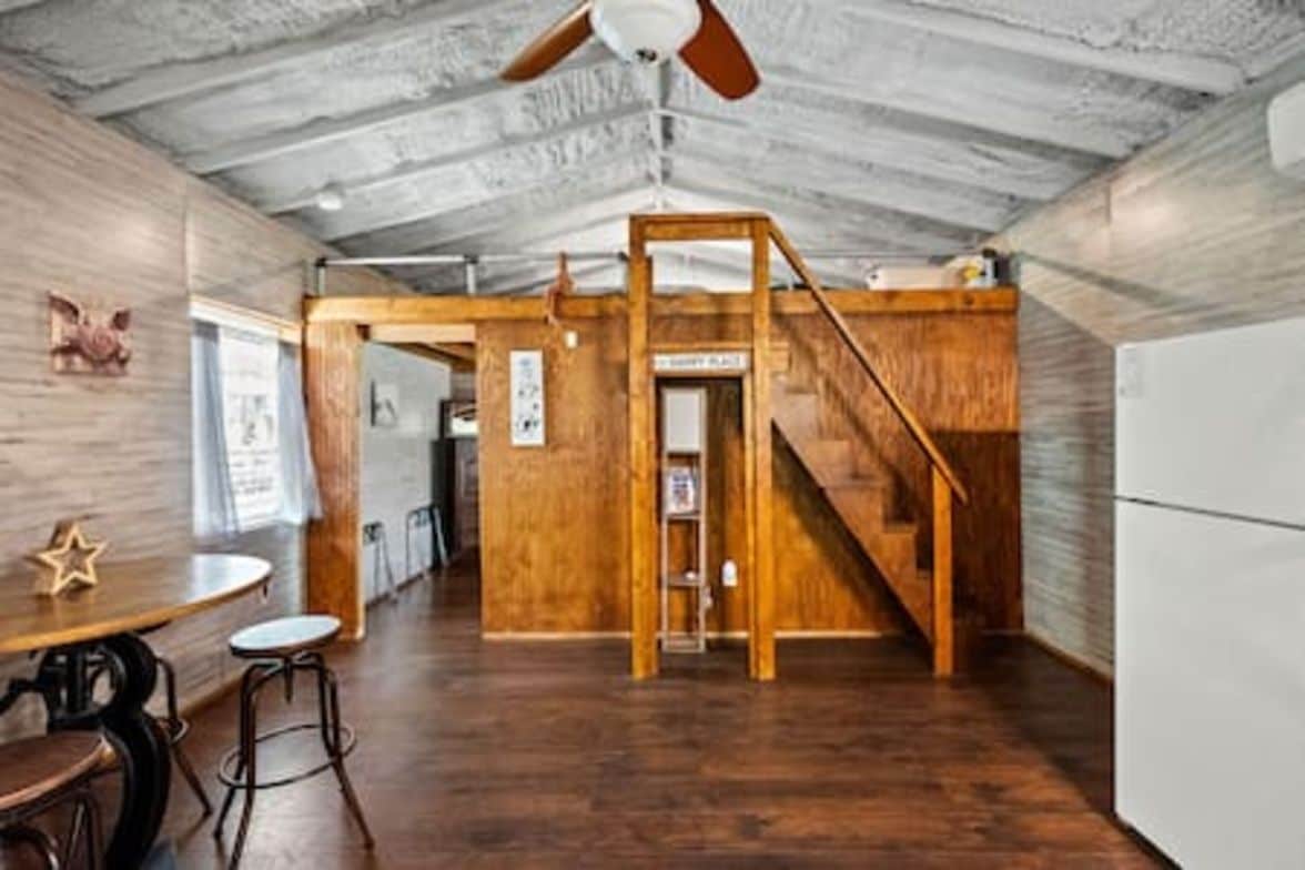 A spacious room with a wooden floor, a ceiling fan, and a staircase leading to an upper level.