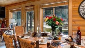 A wooden interior with a dining table set for four, surrounded by wicker chairs, a large window with a view, and a wall-mounted clock. - Abode at Black Bear #104, private hot tub, pool & gym, Deer Valley (Park City)
