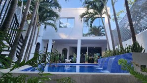 A modern building with a swimming pool, surrounded by palm trees and plants.