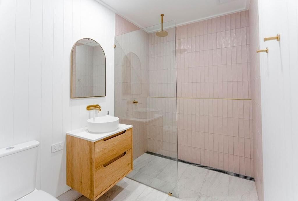 Un bagno moderno con un mobile bagno bianco, uno specchio rotondo e cabina doccia in vetro.