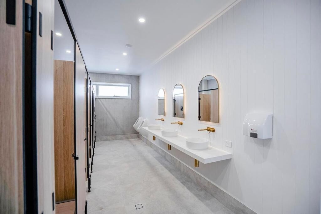 A modern bathroom with three sinks, each with a gold faucet and a mirror above.