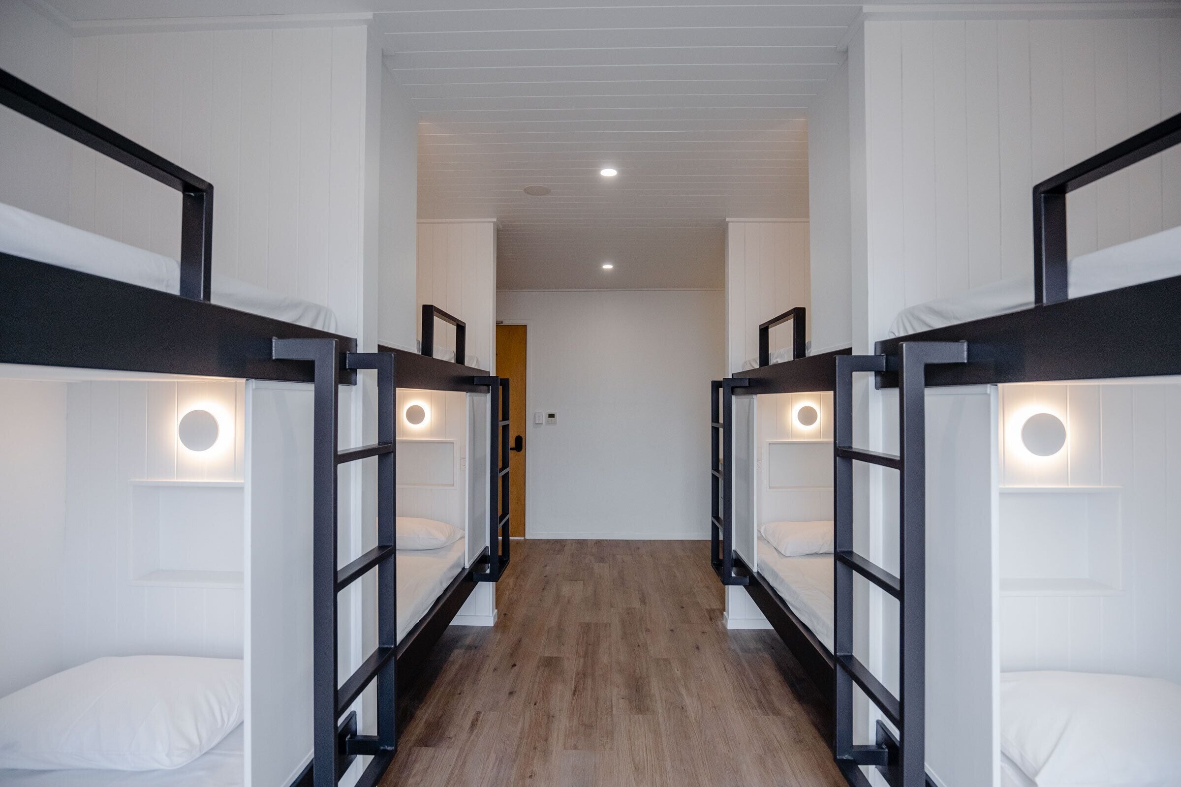 A corridor with bunk beds on either side, each with a circular light fixture.