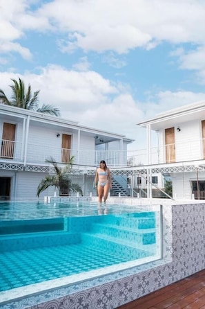 A swimming pool area with a person walking by, surrounded by white buildings with balconies and palm trees. - Bounce Noosa (Sunshine Coast)
