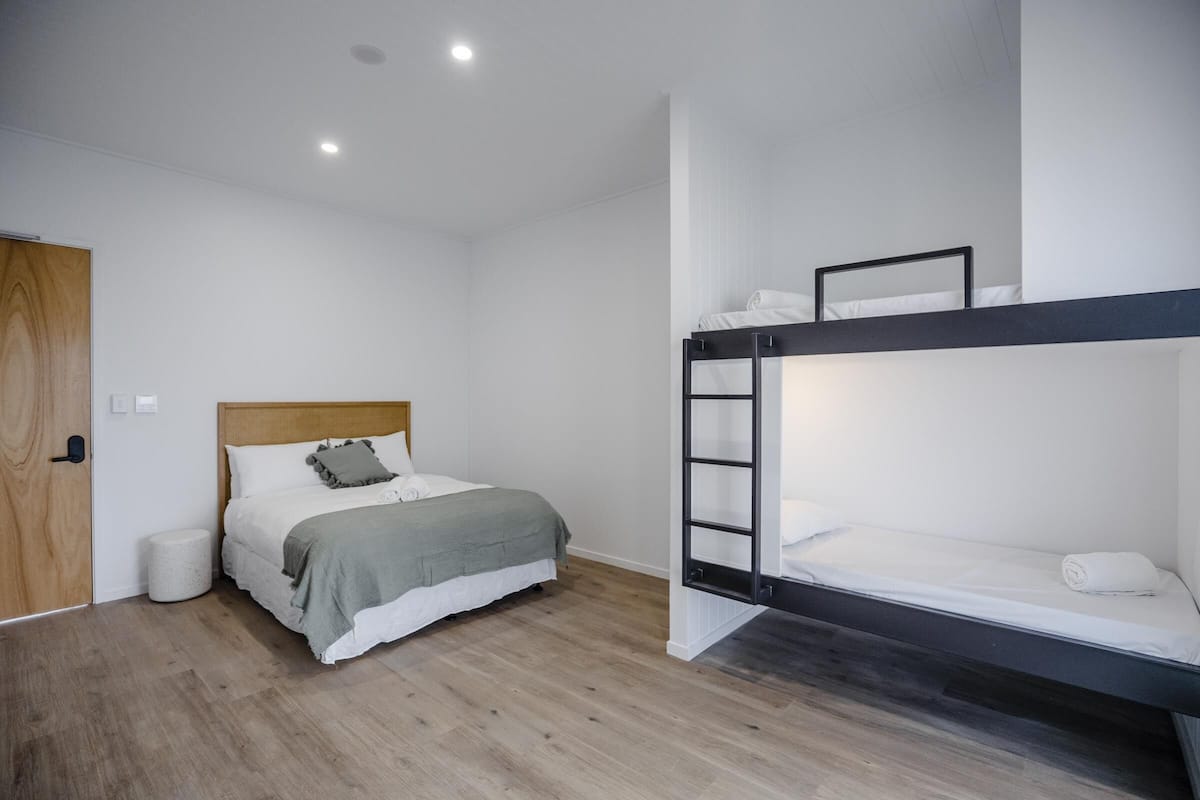 A modern bedroom with a bunk bed, a wooden door, and a small round trash bin.