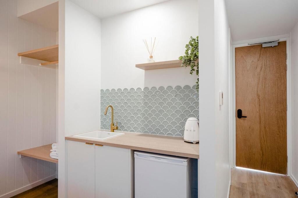 A modern kitchen with white cabinets, a beige countertop, a sink with a gold faucet, and a white coffee maker.