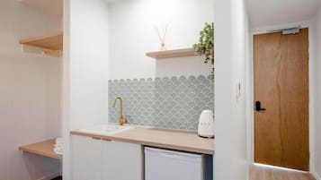 A modern kitchen with white cabinets, a beige countertop, a sink with a gold faucet, and a white coffee maker.