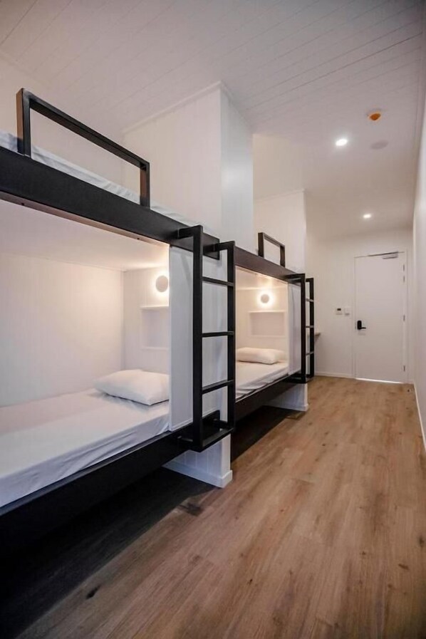 A room with three bunk beds, each with a ladder and a small shelf. The room has white walls and a wooden floor. - Bounce Noosa (Sunshine Coast)