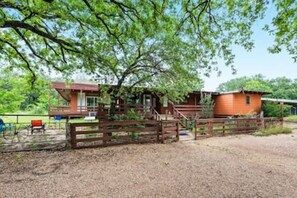 A rustic cabin with a wooden deck, a covered porch, and a fenced yard.