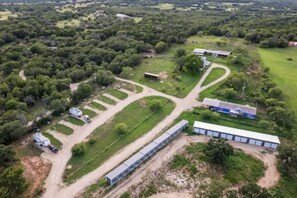 Oversigtsbillede af en ejendom med en lang bygning, flere parkeringsområder og grøn bevoksning omkring.