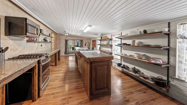 Cozinha moderna com piso de madeira, ilha central, eletrodomésticos embutidos e prateleiras abertas.