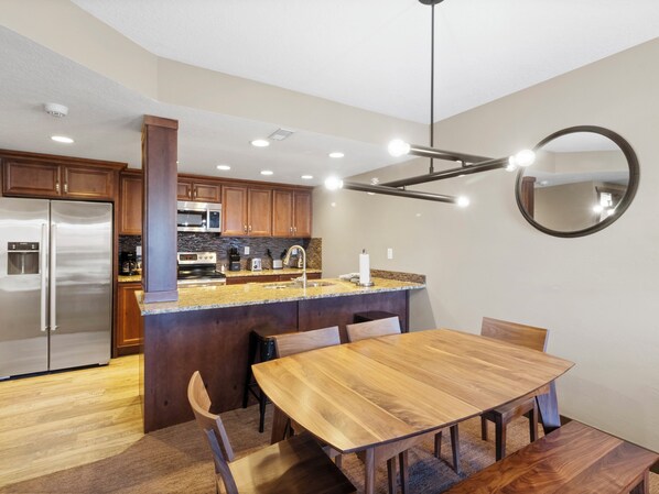 A modern kitchen with a central island, stainless steel appliances, and a dining area with a wooden table and chairs. - Shadow Ridge 305 | Walk to Lifts | Mtn Views | Kitchen | Fireplace | Updated | Pool & Hot Tub (Park City)