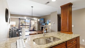 A modern kitchen with granite countertops, stainless steel sink, wooden cabinets, and a dining area with a view. - Shadow Ridge 305 | Walk to Lifts | Mtn Views | Kitchen | Fireplace | Updated | Pool & Hot Tub (Park City)