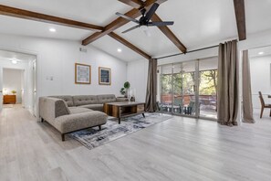 Een ruime woonkamer met een hoekbank, een salontafel en een grote schuifpui naar een terras.