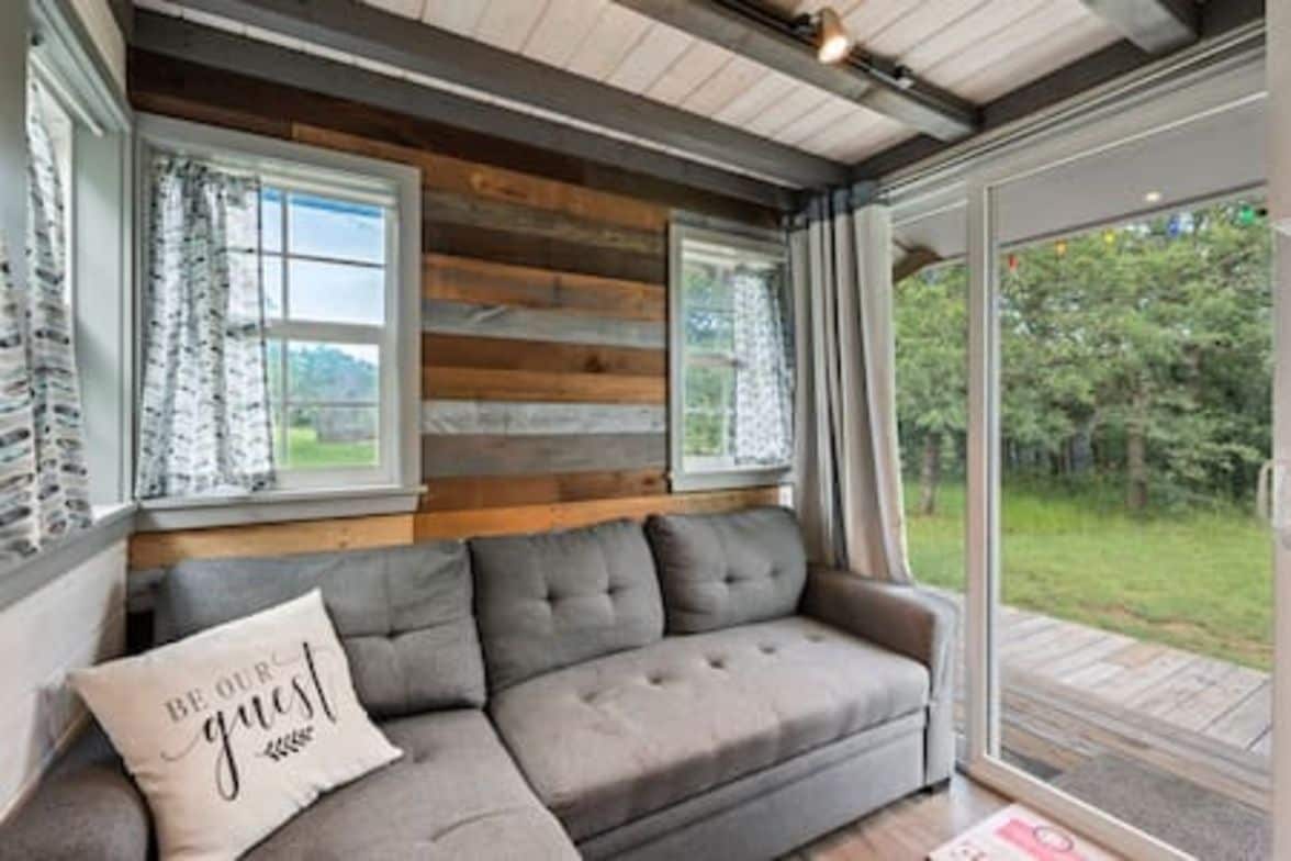 A modern interior with a grey sofa, wooden panel walls, and a glass door leading to an outdoor area.