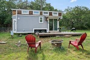 Une petite maison mobile d’un seul étage, dotée d’une terrasse, de deux chaises rouges et d’un foyer extérieur.