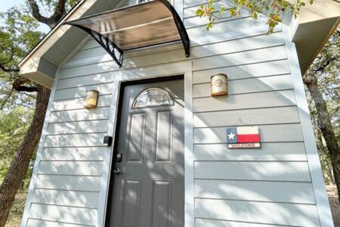 Un edificio pequeño con una puerta gris, un letrero de bienvenida y una bandera de Texas.