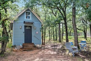 A small blue cabin with a front door and steps leading up to it, surrounded by trees.