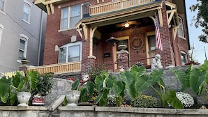A two-story house with a green roof, a front porch, and a stone staircase leading to the entrance.