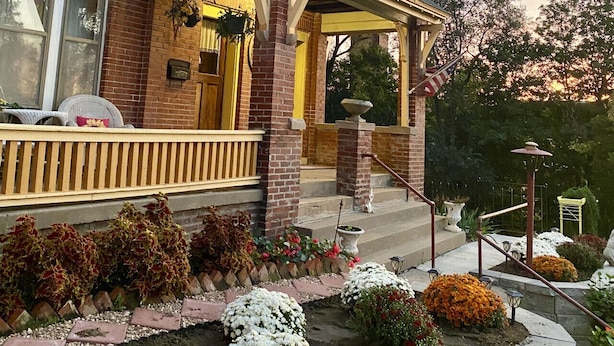 A two-story house with a porch, brick exterior, and a garden with various plants and flowers.