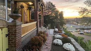 A brick building with a porch, a yellow door, and a garden with white flowers and shrubs.