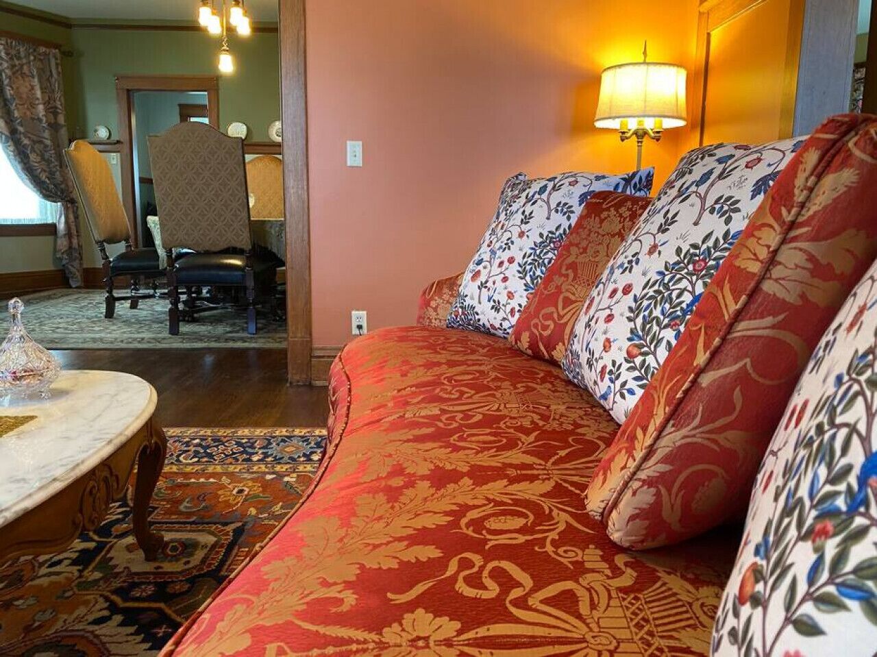 Un salon chaleureux avec un canapé rouge à motifs, des coussins à fleurs, une table basse ronde et un tapis à motifs.