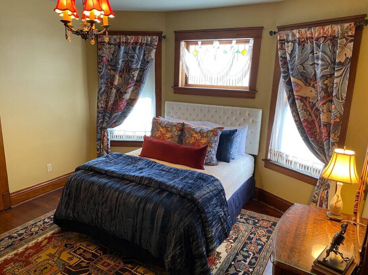 A bedroom with a bed, patterned curtains, a chandelier, and a rug.