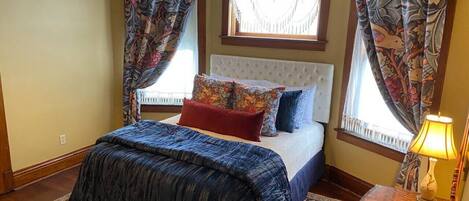 A bedroom with a bed, patterned curtains, a chandelier, and a rug.