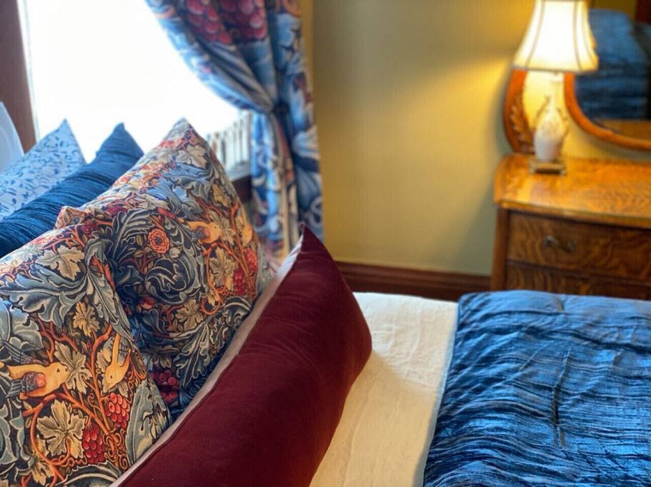 A bed with patterned pillows, a red accent pillow, and a blue bedspread.