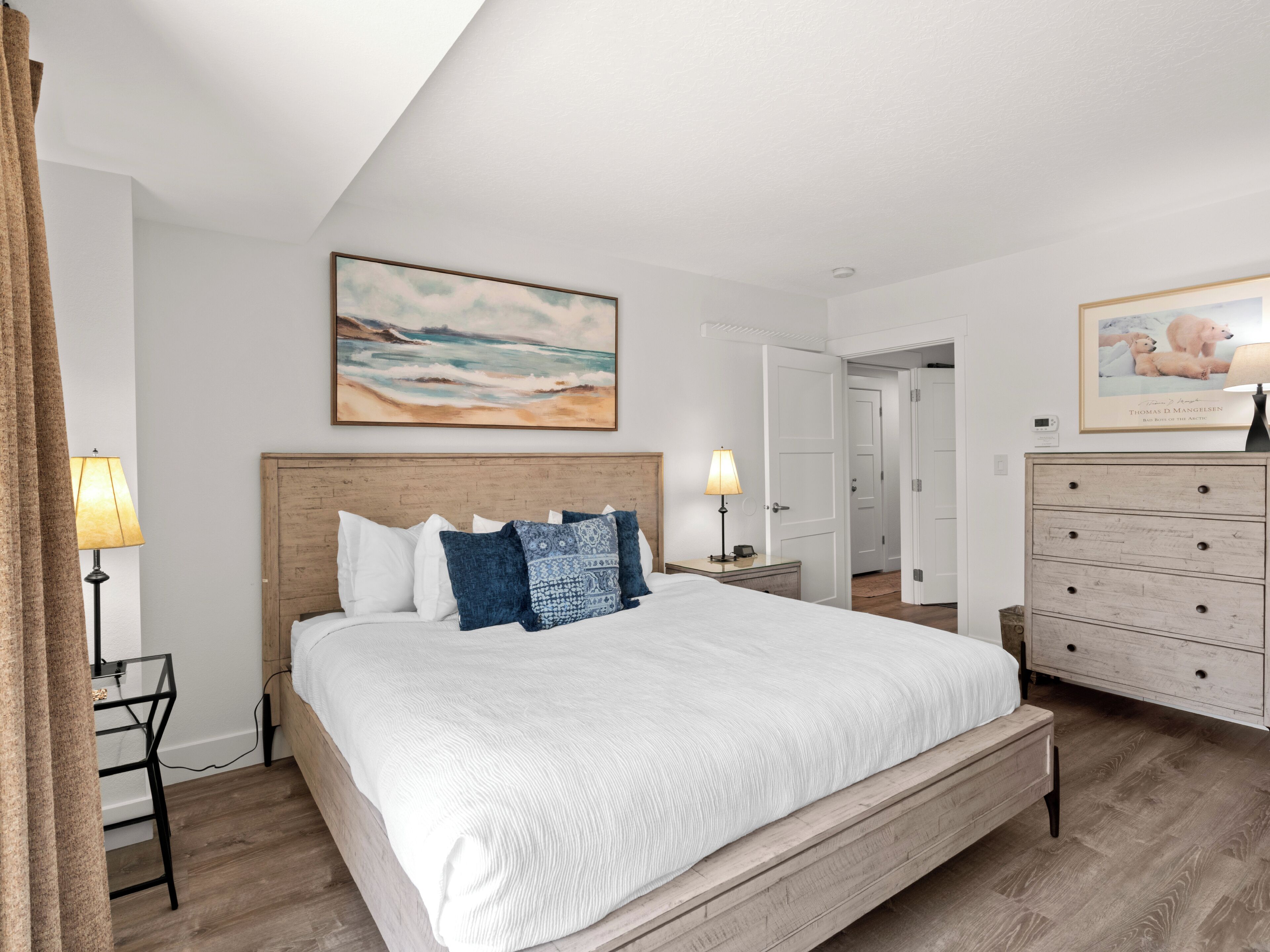 A bedroom with a large bed, a wooden dresser, and two paintings on the walls.