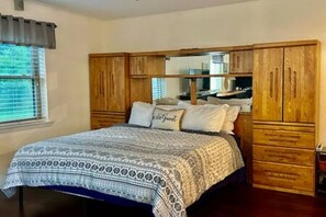 A bedroom with a bed, wooden wardrobe, and a mirror. - FW Studio | Pool + Desk | Near TX Speedway (Fort Worth)