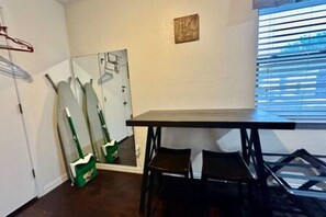A room with a table, two chairs, a mirror, and a window with blinds. - FW Studio | Pool + Desk | Near TX Speedway (Fort Worth)