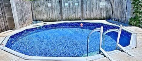 Une piscine entourée d’une clôture en bois et dotée d’un escalier en métal.