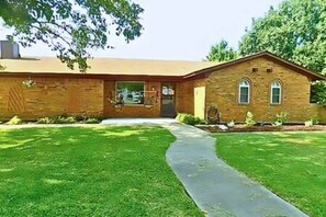 A two-story brick building with a front entrance, a small porch, and a well-maintained lawn. - FW Studio | Pool + Desk | Near TX Speedway (Fort Worth)
