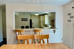 A dining area with a wooden table and chairs, a built-in bench, and a kitchen area visible through a large mirror. - FW Pool + Arcade - Fun Near TX Speedway (Fort Worth)