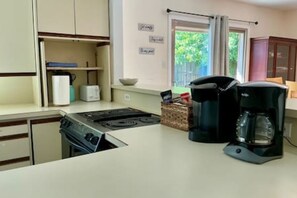 A compact kitchen with a stove, coffee maker, and a small window.